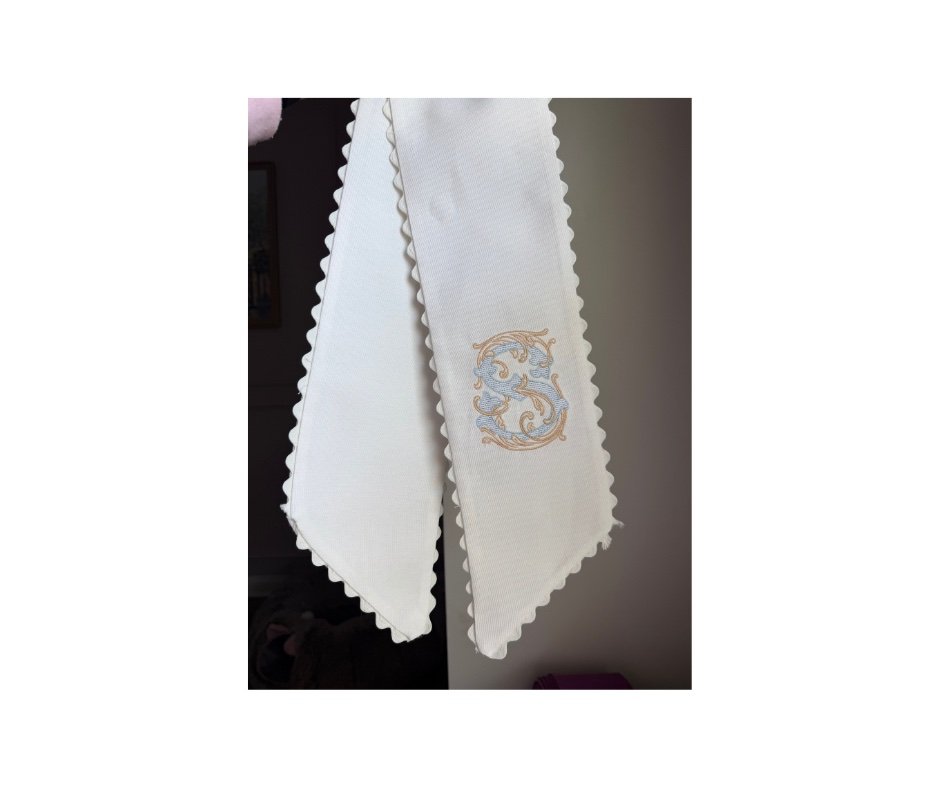 White scalloped-edge wreath sash with blue and gold filigree S monogram